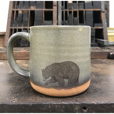 A moss green-colored ceramic mug with an image of a bear imprinted on the front.