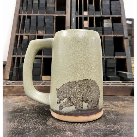 A moss green-colored ceramic stein with an image of a bear imprinted on the front.