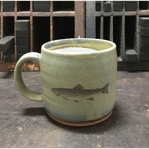 A light green ceramic mug with an image of a brook trout imprinted on the front.