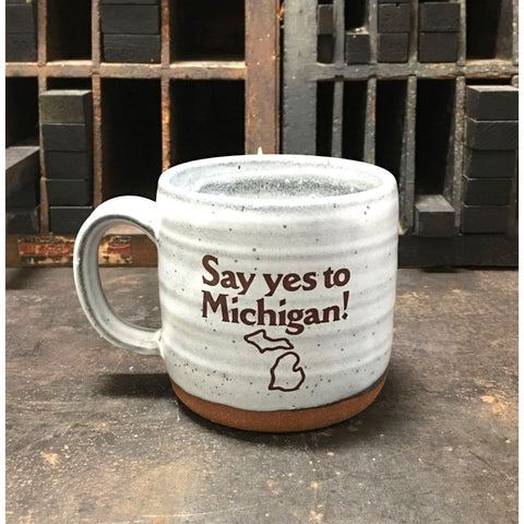A gray ceramic mug with the logo for Say yes to Michigan! imprinted on the front.