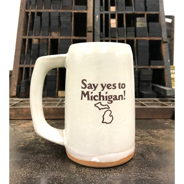 A cream-colored ceramic stein with the logo for Say yes to Michigan! imprinted on the front.