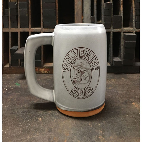 A light gray ceramic stein with the label for Wolverine Beer produced by Wolverine Brewing Company imprinted on the front.