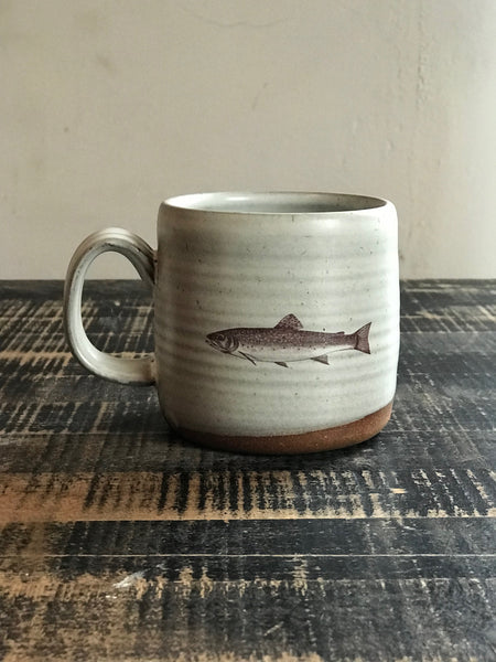A light gray ceramic mug with an image of a brook trout imprinted on the front. 