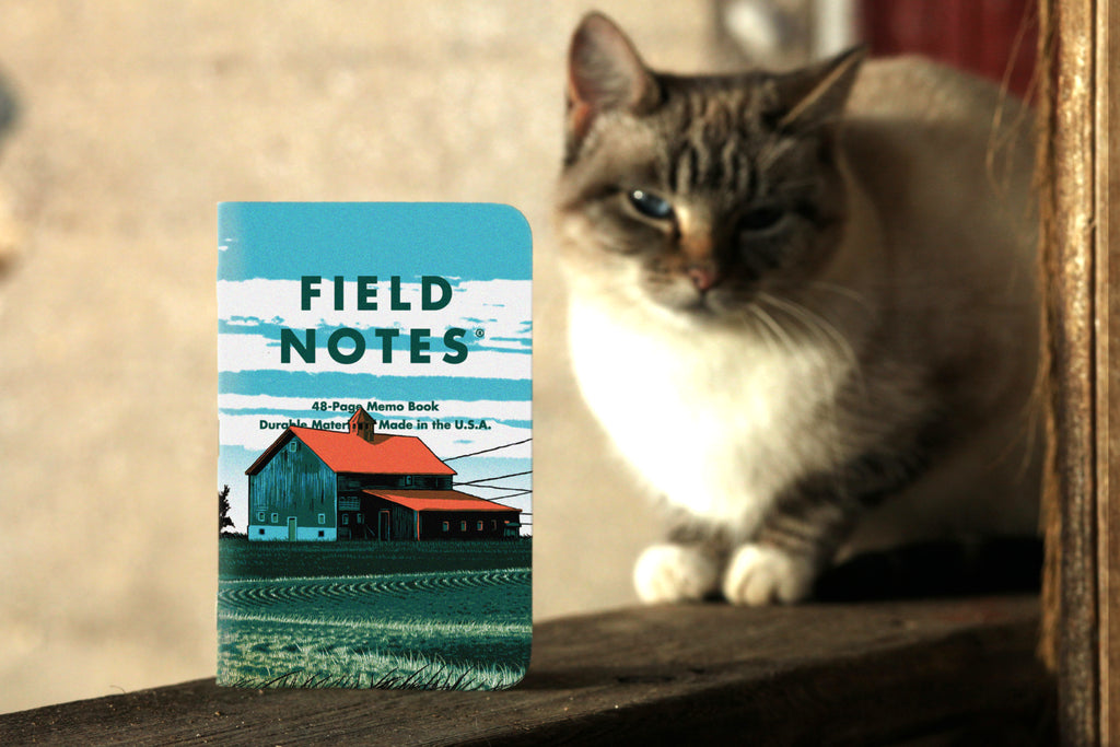 Front of Field Notes Heartland notebook featuring a farm house. There is a cat in the background behind the notebook.