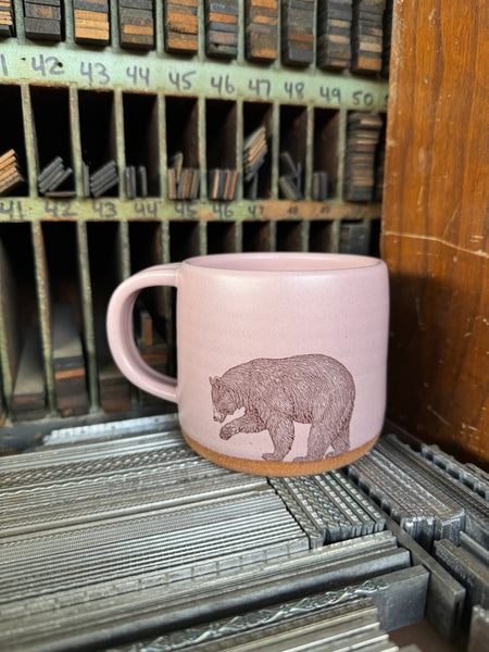 A rose-colored ceramic mug with an image of a bear imprinted on the front.