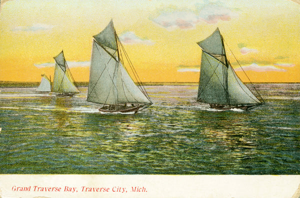 Front of a historical postcard featuring four sailboats in the water with a yellow sky behind them. Text on the bottom reads “Grand Traverse Bay, Traverse City, Mich.”