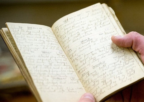 Hands holding a small notebook with handwritten notes across both pages.