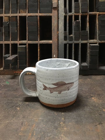 A gray ceramic mug with an image of a grayling imprinted on the front. 