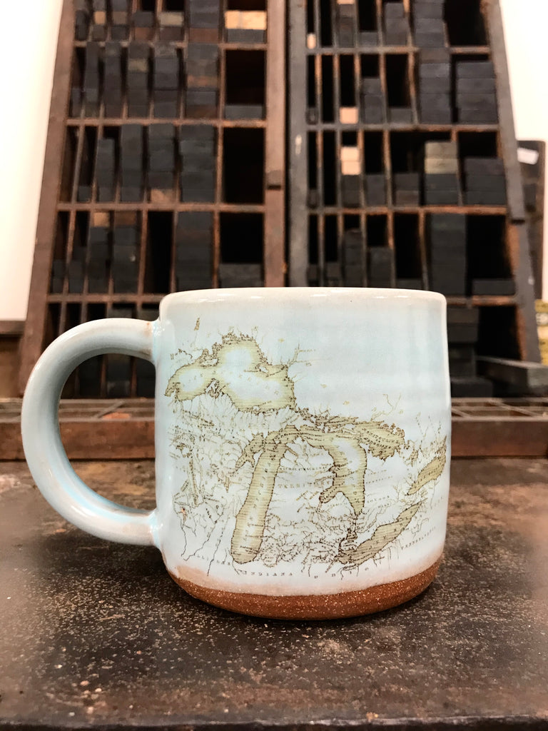 A gray ceramic mug with a historical map of Michigan imprinted on the front.