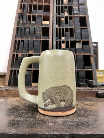 A moss green-colored ceramic stein with an image of a bear imprinted on the front. 
