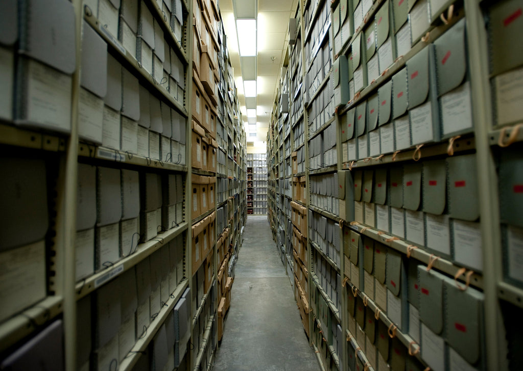 Photograph looks down a long aisle of metal shelving filled to the brim with archival boxes.
