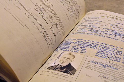 Open book photographed at angle. One page is a naturalization record but text is illegible. There is a picture of an older man at the bottom of the page.