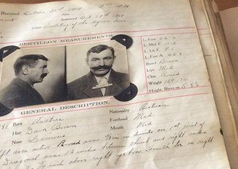 A photograph of an old volume. The page displays a mugshot photo of a man photographed from the side and front. The man has a substantial mustache. Notes are made on the page although illegible there are headings of "Bertillon Measurements" and "General Description."