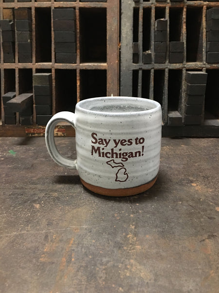 A gray ceramic mug with the logo for Say yes to Michigan! imprinted on the front. 