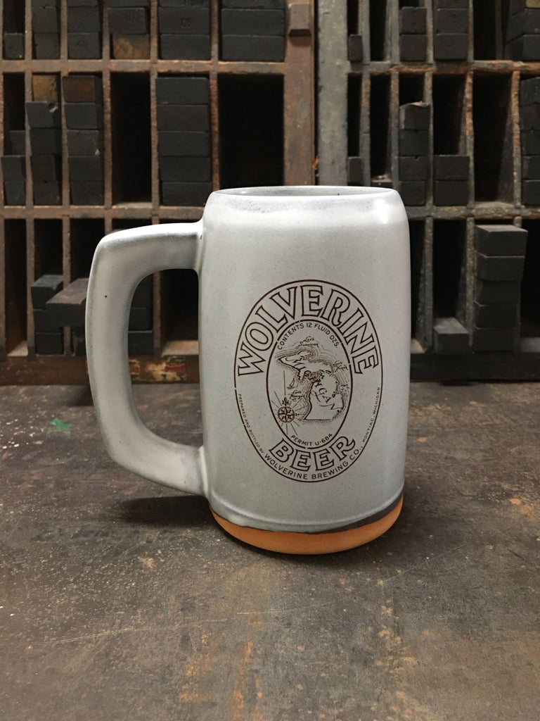 A light gray ceramic stein with the label for Wolverine Beer produced by Wolverine Brewing Company imprinted on the front. 