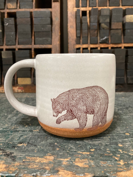 A cream-colored ceramic mug with an image of a bear imprinted on the front.