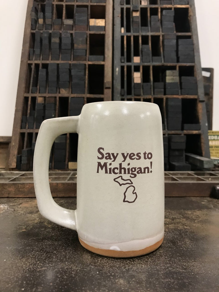 A cream-colored ceramic stein with the logo for Say yes to Michigan! imprinted on the front. 